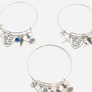 Peut inclure: Trois bracelets en argent avec un charme en forme de c&oelig;ur qui dit "You are always in my heart!" Chaque bracelet a un charme en forme de croix, un charme en forme d'aile d'ange et un charme en forme d'ange qui dit "Angels Watching Over Me".