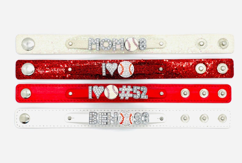 May include: Four sparkly bracelets with rhinestones and a baseball charm. The bracelets are white, red, and red glitter. The charms say "MOM", "I LOVE", "I LOVE #52", and "BEN#91".