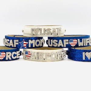 May include: Six different blue and white leather bracelets with rhinestones and American flag charms. The bracelets say "Air Force", "USAF Mom", "USAF Wife", "I Love USA", "Air Force", and "I Love USA".