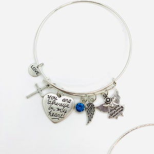 Peut inclure: Bracelet en argent avec un charme en forme de c&oelig;ur qui dit "Tu es toujours dans mon c&oelig;ur", un charme en forme de croix, un charme en cristal bleu, un charme en forme d'aile et un charme en forme d'ange qui dit "Les anges veillent sur moi".