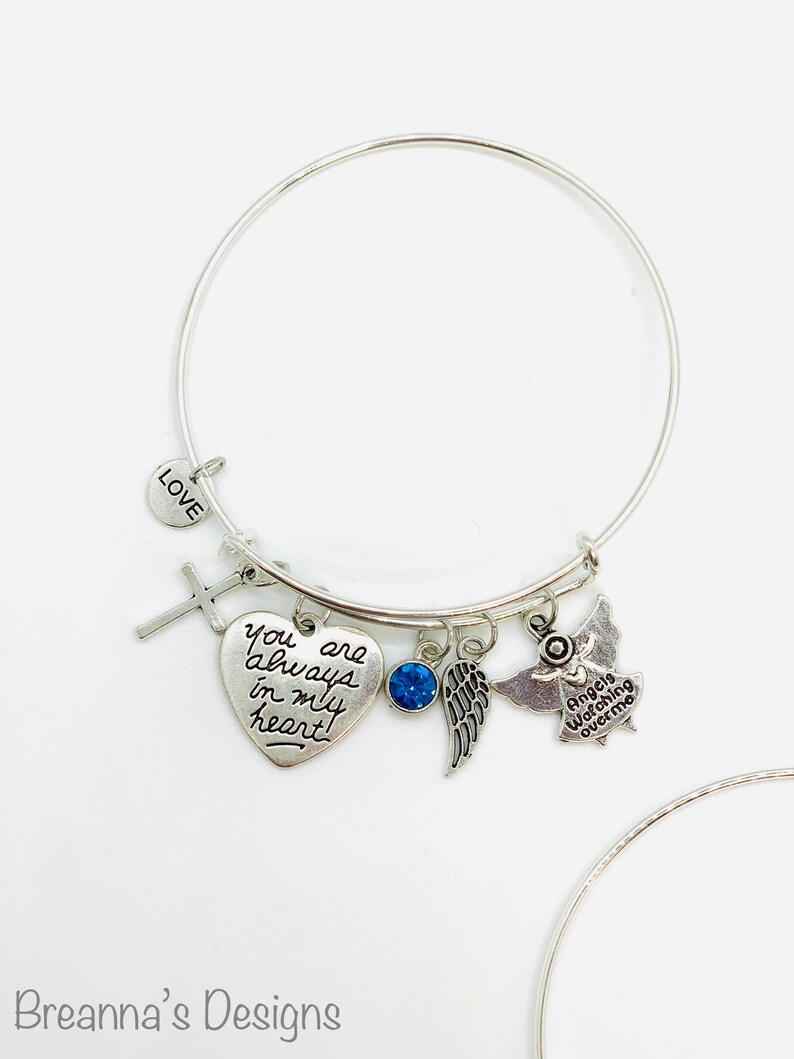 Peut inclure: Bracelet en argent avec un charme en forme de c&oelig;ur qui dit "Tu es toujours dans mon c&oelig;ur", un charme en forme de croix, un charme en cristal bleu, un charme en forme d'aile et un charme en forme d'ange qui dit "Les anges veillent sur moi".