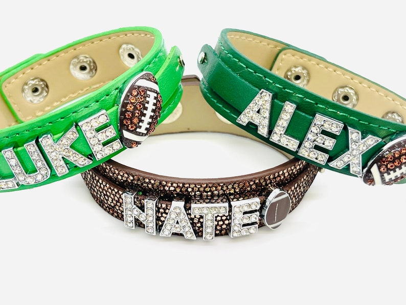 May include: Three green leather bracelets with rhinestones spelling out the names "LUKE", "ALEX", and "NATE". Each bracelet has a brown football charm.