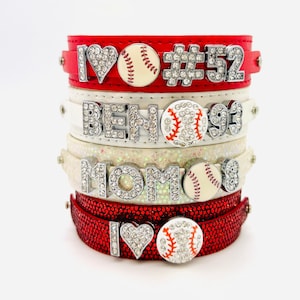 May include: Stack of four red and white leather bracelets with rhinestones and baseball charms. The bracelets feature the text "I love", "#52", "BEN", "MOM", and a baseball with rhinestones.