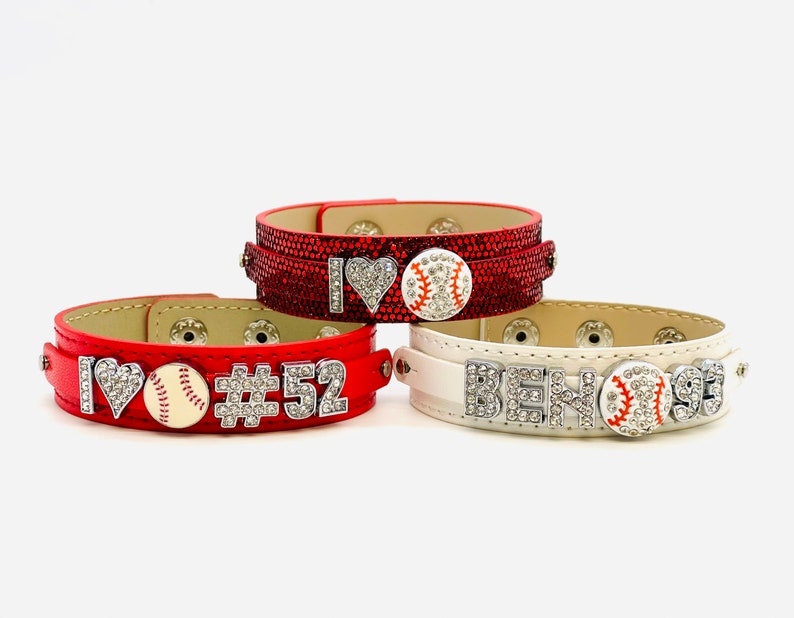 May include: Three adjustable snap bracelets with rhinestones. The red bracelet has a heart, baseball, and the text "I #52". The white bracelet has the text "BEN#93".