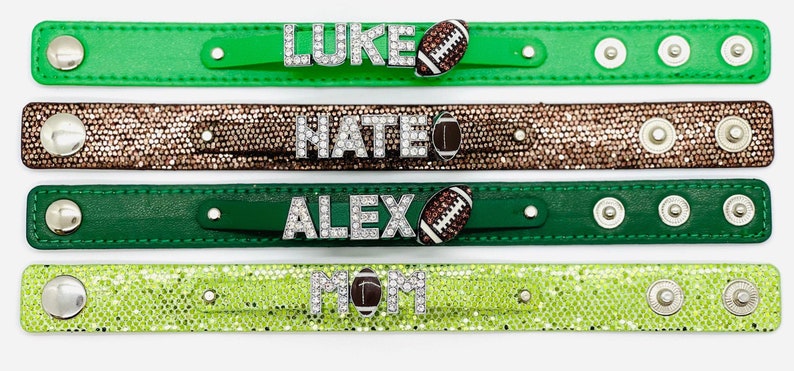 May include: Four green, brown, and lime green leather bracelets with rhinestones spelling out the names "LUKE", "NATE", "ALEX", and "MOM" with a football charm on each.