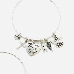 Peut inclure: Bracelet en argent avec un charme en forme de c&oelig;ur qui dit "You are always in my heart!" et d'autres charmes, dont une croix, une lettre K, une aile et un ange avec le texte "Angels watching over me".