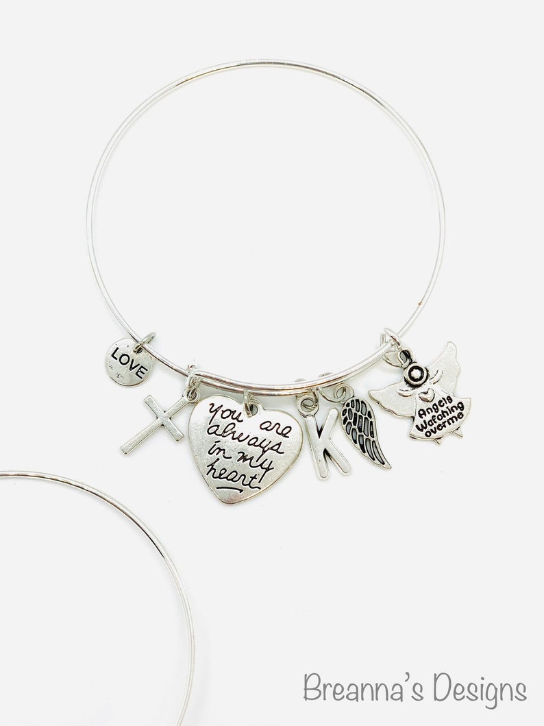 Peut inclure: Bracelet en argent avec un charme en forme de c&oelig;ur qui dit "You are always in my heart!" et d'autres charmes, dont une croix, une lettre K, une aile et un ange avec le texte "Angels watching over me".