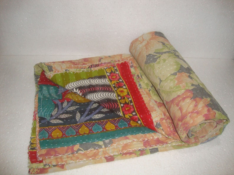 May include: A colorful, patchwork quilt with floral and geometric patterns. The quilt features a rolled section revealing a large floral print in shades of peach, green, and gray. The folded section displays a variety of patterns and colors.