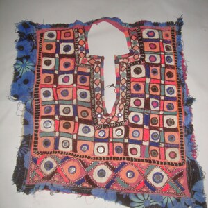 May include: A colourful embroidered fabric panel with a geometric pattern of squares and circles. The fabric is decorated with small mirrors and beads. The panel has a fringed edge and is made of a dark blue fabric with floral designs.