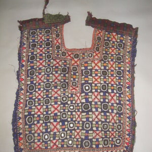 May include: A colorful embroidered fabric panel with a geometric pattern and small round mirrors. The fabric is a dark blue color with red, green, white, and orange accents. The panel is likely a traditional garment piece.