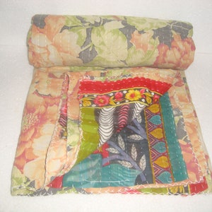 May include: A rolled-up floral quilt with a patchwork design. The quilt features large peach and green floral patterns, with a section of colorful patchwork including red, green, and patterned fabrics. White stitching is visible throughout.