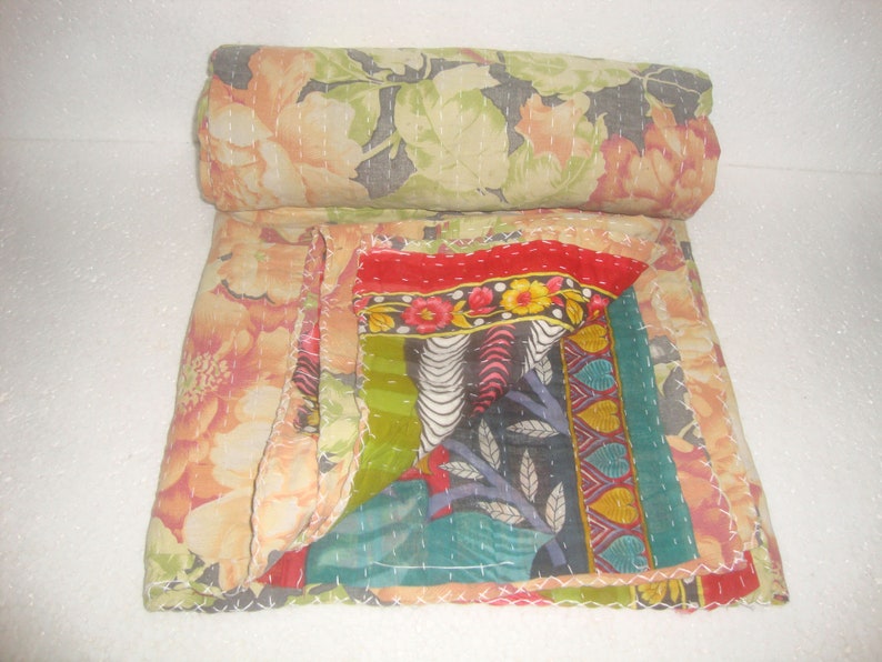 May include: A rolled-up floral quilt with a patchwork design. The quilt features large peach and green floral patterns, with a section of colorful patchwork including red, green, and patterned fabrics. White stitching is visible throughout.