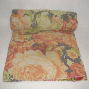 May include: Rolled floral quilt featuring large peach and cream-colored flowers with green leaves on a dark gray background. The quilt is hand-stitched with white thread, showcasing a detailed floral pattern.