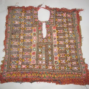 May include: A vintage embroidered fabric panel with a geometric pattern and colorful beads and mirrors. The fabric is a cream color with a red border and is in good condition.