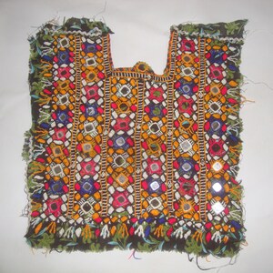 May include: A colourful embroidered fabric panel with a geometric pattern and small mirrors. The fabric is black with red, blue, green, yellow, and white embroidery. The panel is fringed on all sides.