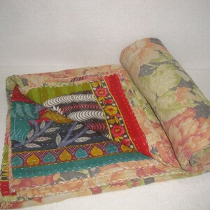 May include: A colorful, patchwork quilt with floral and geometric patterns. The quilt features a rolled section revealing a large floral print in shades of peach, green, and gray. The folded section displays a variety of patterns and colors.