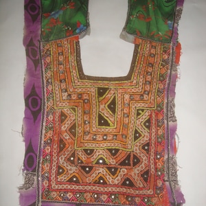 May include: A colourful embroidered neckline with a geometric pattern and mirrored accents. The neckline is made of fabric with a purple, green, and orange colour scheme.