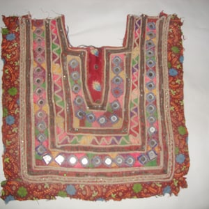 May include: A colourful embroidered fabric panel with a geometric design and small mirrors. The fabric is a mix of red, brown, green, blue, and pink.
