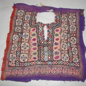 May include: A purple, red, and white embroidered fabric panel with a decorative neckline. The fabric is adorned with colorful geometric patterns and small mirrors.
