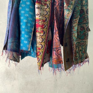 K&ouml;nnte beinhalten: Eine Sammlung von f&uuml;nf rechteckigen Stoff&uuml;berw&uuml;rfen, die an einer Leine h&auml;ngen, jeder mit unterschiedlichen Mustern wie Paisley, Blumen und geometrischen Motiven in leuchtenden Blau-, Rot-, Orange-, Gr&uuml;n- und Gelbt&ouml;nen mit sichtbaren Steppstichdetails.