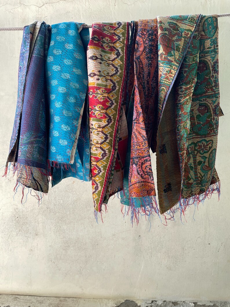 K&ouml;nnte beinhalten: Eine Sammlung von f&uuml;nf rechteckigen Stoff&uuml;berw&uuml;rfen, die an einer Leine h&auml;ngen, jeder mit unterschiedlichen Mustern wie Paisley, Blumen und geometrischen Motiven in leuchtenden Blau-, Rot-, Orange-, Gr&uuml;n- und Gelbt&ouml;nen mit sichtbaren Steppstichdetails.