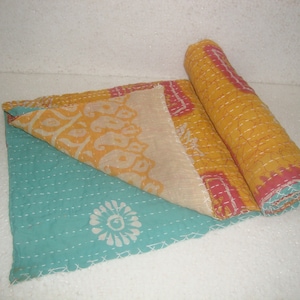 May include: A hand-stitched kantha quilt with a turquoise blue background and a yellow, pink, and white floral pattern. The quilt is folded in half and rolled up.