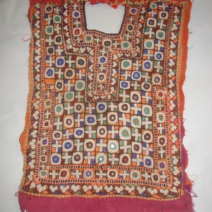 May include: A red, white, and blue embroidered fabric panel with a geometric pattern of circles and crosses. The fabric is decorated with small, round mirrors.