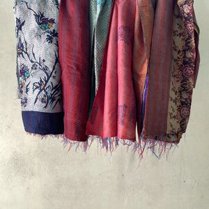 K&ouml;nnte beinhalten: Eine Sammlung rechteckiger Stoff&uuml;berw&uuml;rfe mit komplexen Kantha-N&auml;hten und verschiedenen Mustern, darunter florale Motive, geometrische Designs und kr&auml;ftige Rott&ouml;ne, die mit ausgefransten Kanten versehen sind und an einer horizontalen Leine h&auml;ngen.