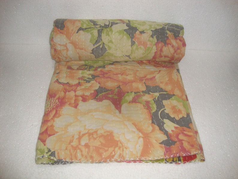 May include: Rolled floral quilt featuring large peach and cream-colored flowers with green leaves on a dark gray background. The quilt is hand-stitched with white thread, showcasing a detailed floral pattern.