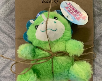Może przedstawiać: Pluszowa zabawka w kształcie zielonego i niebieskiego, puszystego dinozaura, owinięta w brązowy papier ze sznurkiem i etykietą z napisem "Fuzzy Friends". Papier jest oznaczony napisem "Blind Date With! A Children's Book!"