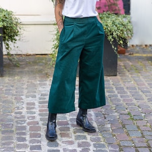 Puede incluir: Culottes de pana verde esmeralda con pernera ancha. Los pantalones tienen cintura alta y bolsillos. Combinados con botines de cuero negro. Una opción elegante y cómoda para el uso diario.
