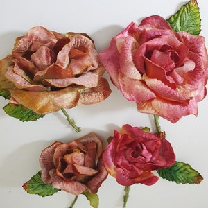 May include: Four artificial silk roses with green leaves. The roses are in shades of pink and orange.