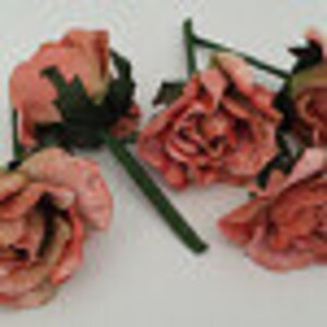 May include: Five pink fabric roses with green stems. The roses are arranged in a cluster, with the stems pointing in different directions.