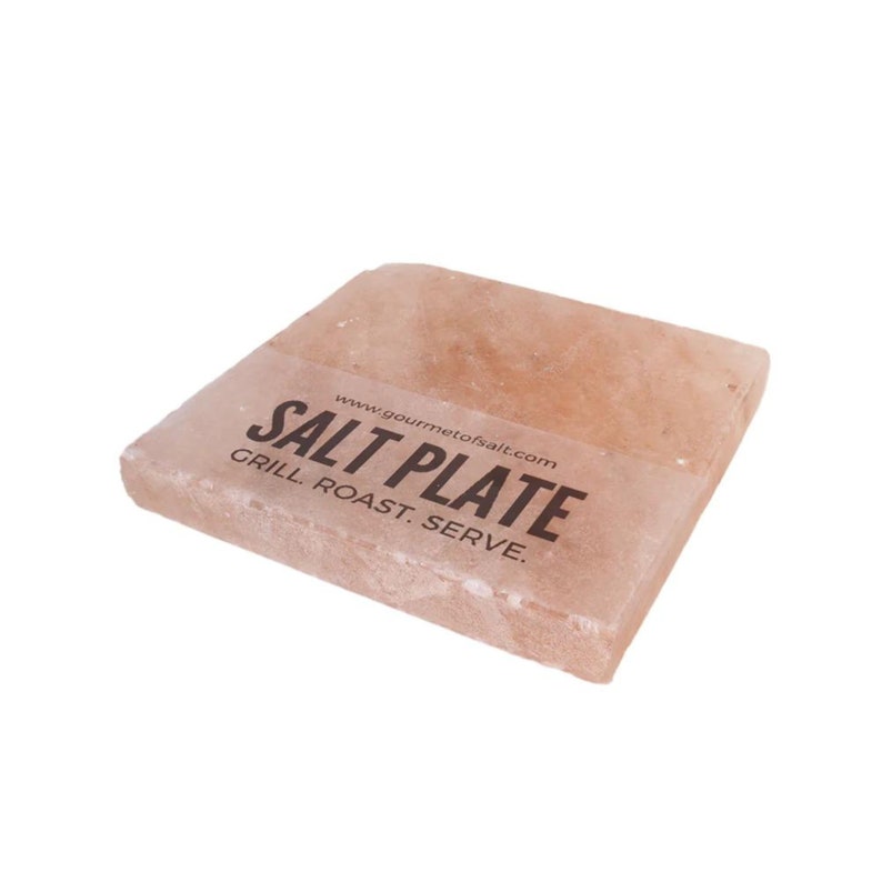 Op de afbeelding: Een roze Himalaya-zoutplaat om te grillen, roosteren en serveren. De plaat heeft een label met de tekst "SALT PLATE" en "www.gourmetofsalt.com".