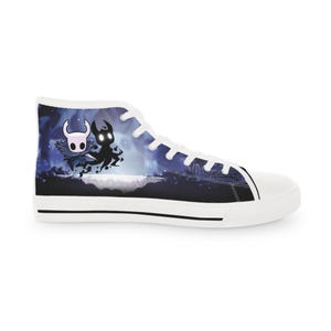 Könnte beinhalten: Ein High-Top-Sneaker mit weißer Gummisohle und weißen Schnürsenkeln. Das Seitenteil zeigt einen dunkelblauen und schwarzen Grafikdruck, der eine weiß maskierte Figur und eine schattenhafte Gestalt vor einem sternenklaren Hintergrund darstellt.