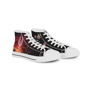 Könnte beinhalten: High-Top-Sneaker mit schwarzem Obermaterial aus Canvas, weißen Schnürsenkeln und Gummikappen. Die Seitenteile zeigen einen Grafikdruck einer rot umhangenen Figur mit weißer Maske und kleinen Kreaturen vor einem dunklen, feurig orangen Hintergrund.