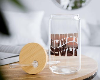 May include: A clear glass can with a bamboo lid and a straw. The can has a graphic of a sunset with the words "Howdy Howdy" printed on it.