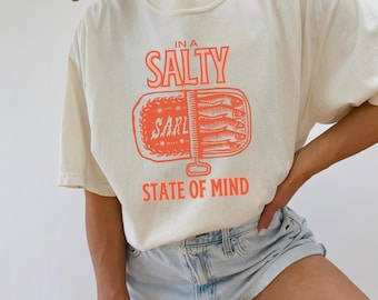 May include: A white t-shirt with a graphic of a can of sardines and the text "In a Salty State of Mind".