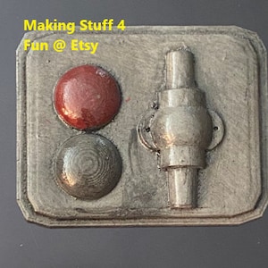May include: A gray metal panel with two round buttons, one red and one gray, and a silver metal lever with a round knob. The panel has a textured surface and the text "Making Stuff 4 Fun @ Etsy" is printed on the top.
