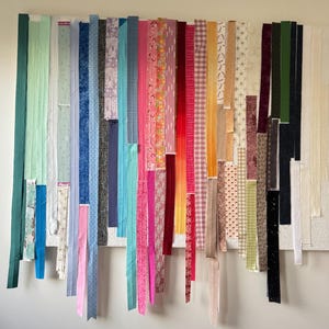 Peut inclure: Présentation de bandes de tissu colorées dans divers motifs et teintes, notamment floraux, géométriques et unis. Les bandes sont disposées verticalement, créant un effet visuel vibrant et texturé. Les tissus sont fixés à un tableau blanc.