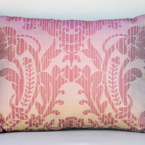 May include: A pink and cream throw pillow with a damask pattern and a burgundy fringe border.