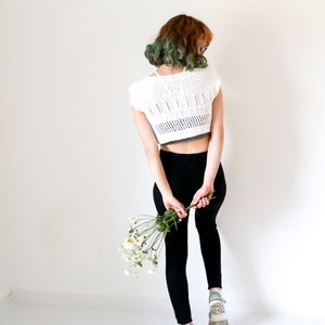 A woman in front of a white wall wearing black leggings and a white shirt.