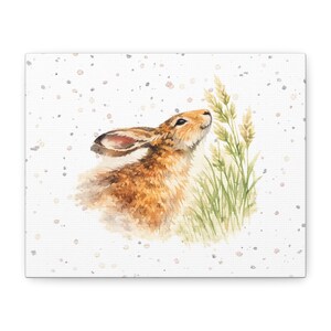 May include: Watercolor painting of a brown hare sniffing tall grass. The hare has long ears and is facing upwards. The background is white with small, speckled dots. The artwork is on a canvas.