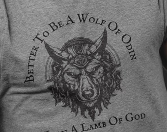 以下が含まれることがあります： オオカミのグラフィックと「Better to be a Wolf of Odin than a Lamb of God」のテキストが入ったグレーのTシャツ。シャツは半袖とクルーネックです。デザインは、角のあるオオカミの頭の精巧なイラストが特徴です。
