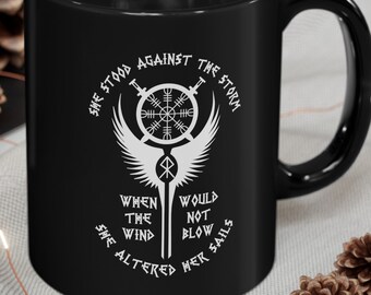 May include: Black coffee mug with a white design featuring a compass, wings, and the text "She stood against the storm when the wind would not blow she altered her sails".