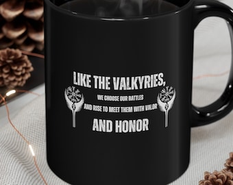 May include: Black coffee mug with white text that reads "Like the Valkyries, we choose our battles and rise to meet them with valor and honor". The text is surrounded by two stylized images of a valkyrie's helmet.