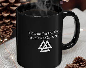 May include: Black coffee mug with white text that reads "I follow the old ways, and the old gods" with a white triquetra symbol below the text.