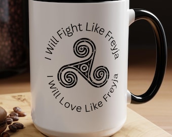 Puede incluir: Taza de cerámica blanca con borde y asa negros. La taza tiene un diseño en blanco y negro con un símbolo triquetra y el texto "I Will Fight Like Freyja I Will Love Like Freyja".