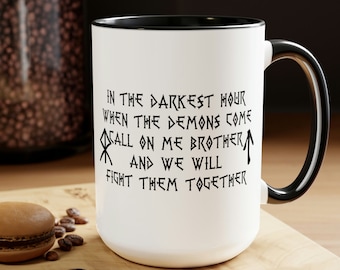 Könnte beinhalten: Weiße Keramiktasse mit schwarzem Rand und Henkel. Die Tasse hat eine schwarze Aufschrift mit dem Text "In der dunkelsten Stunde, wenn die Dämonen kommen, rufe mich Bruder an und wir werden sie gemeinsam bekämpfen".