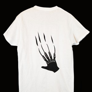 May include: White t-shirt with a black silhouette of a hand with long claws on the back.